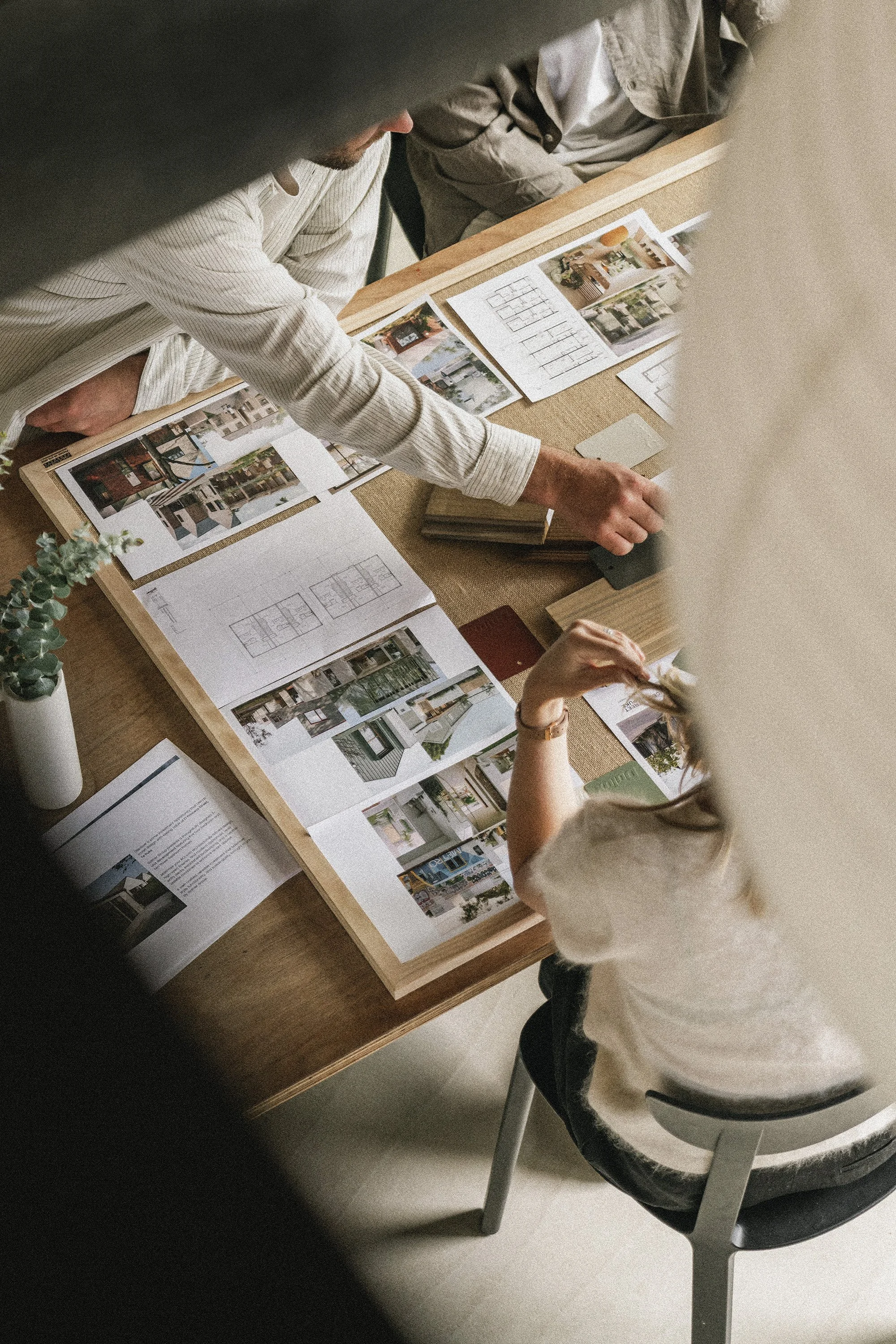 Gather Group team, Hugh and Tim reviewing architectural plans and photographs of building designs on a wooden table, surrounded by documents.