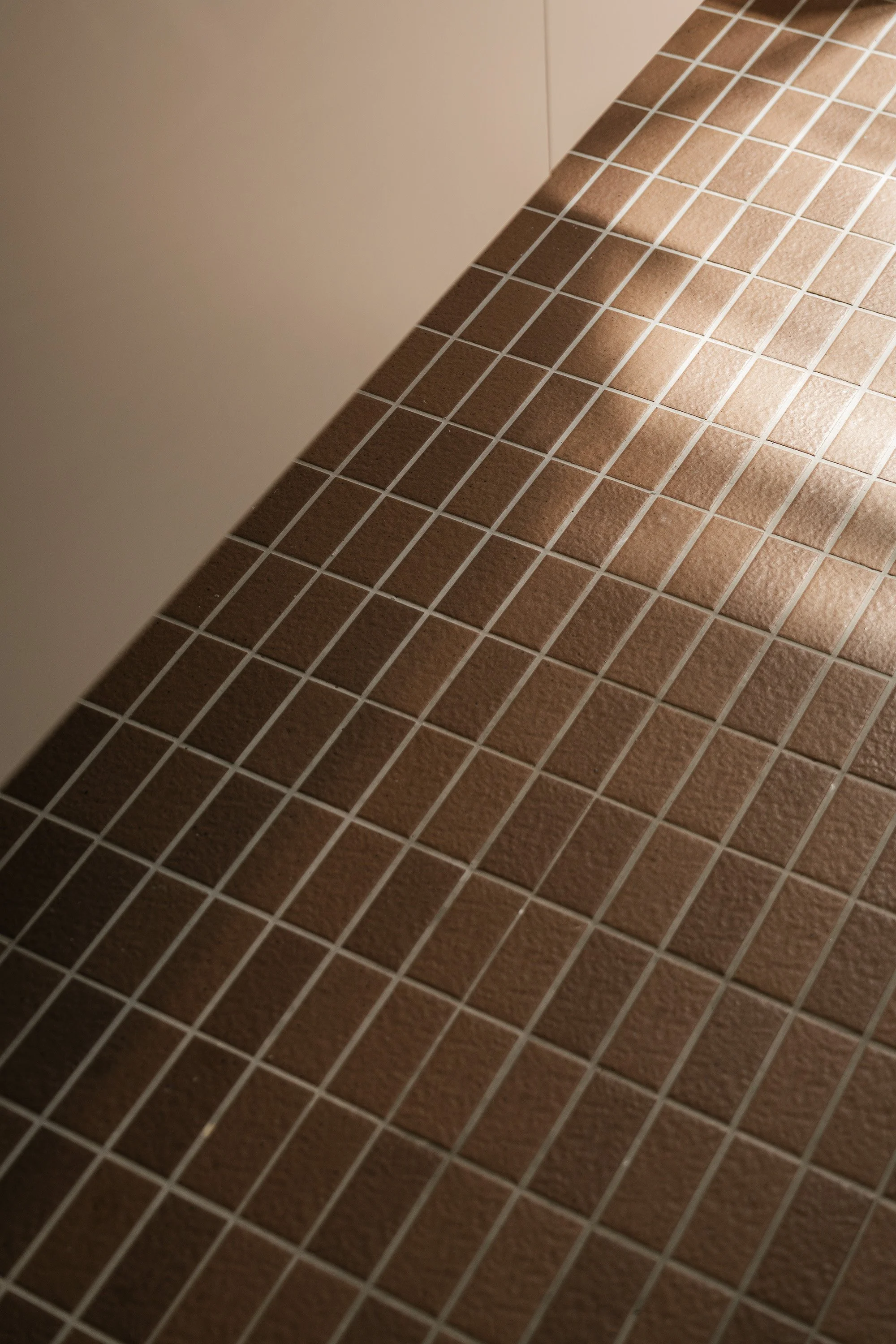 Close-up of brown square tiles on the floor, with a shadow cast over part of the surface.