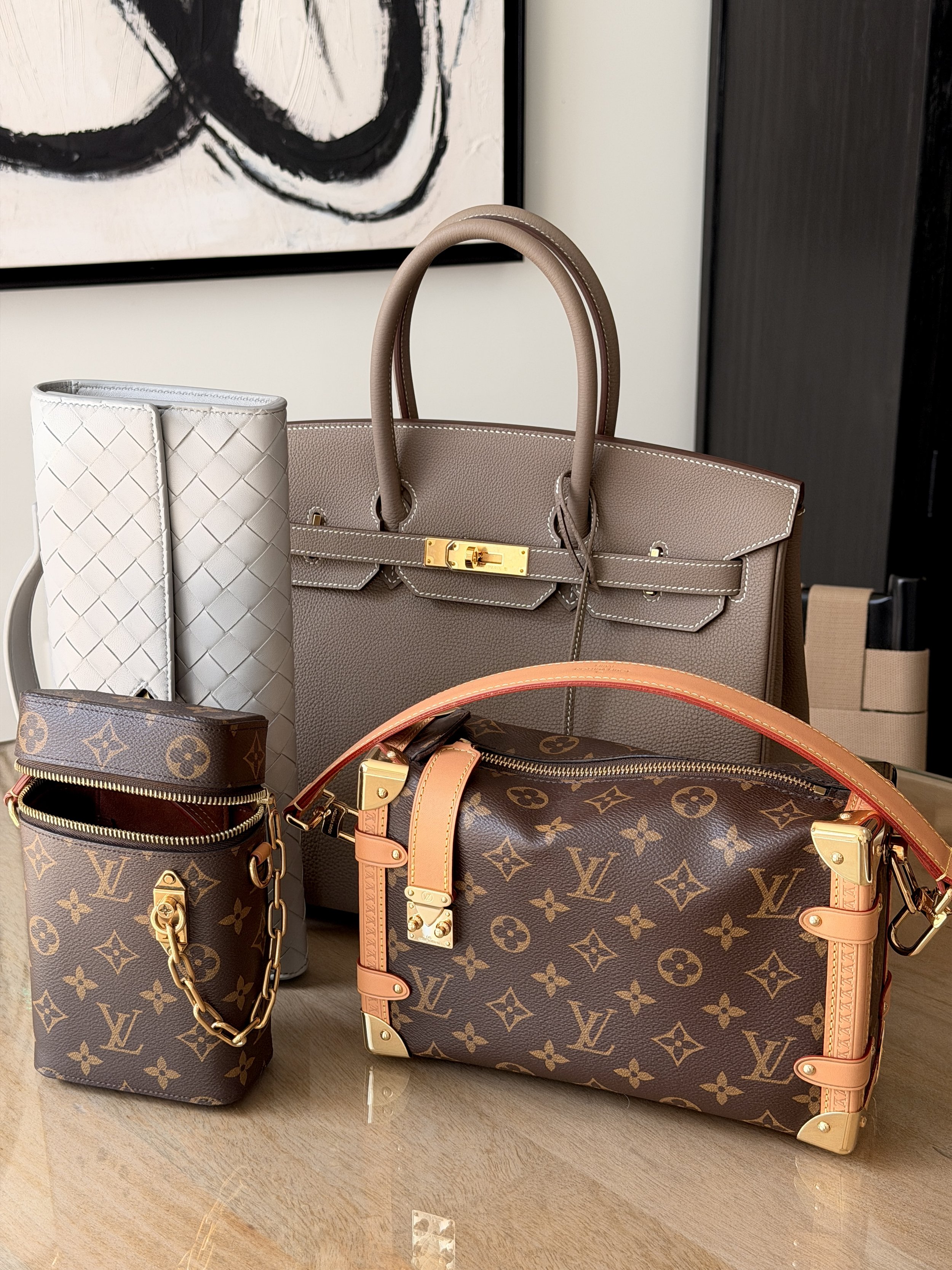 Collection of luxury designer handbags, including Louis Vuitton Monogram tote, small Louis Vuitton designer purse, and a white quilted purse, displayed on a wooden surface.