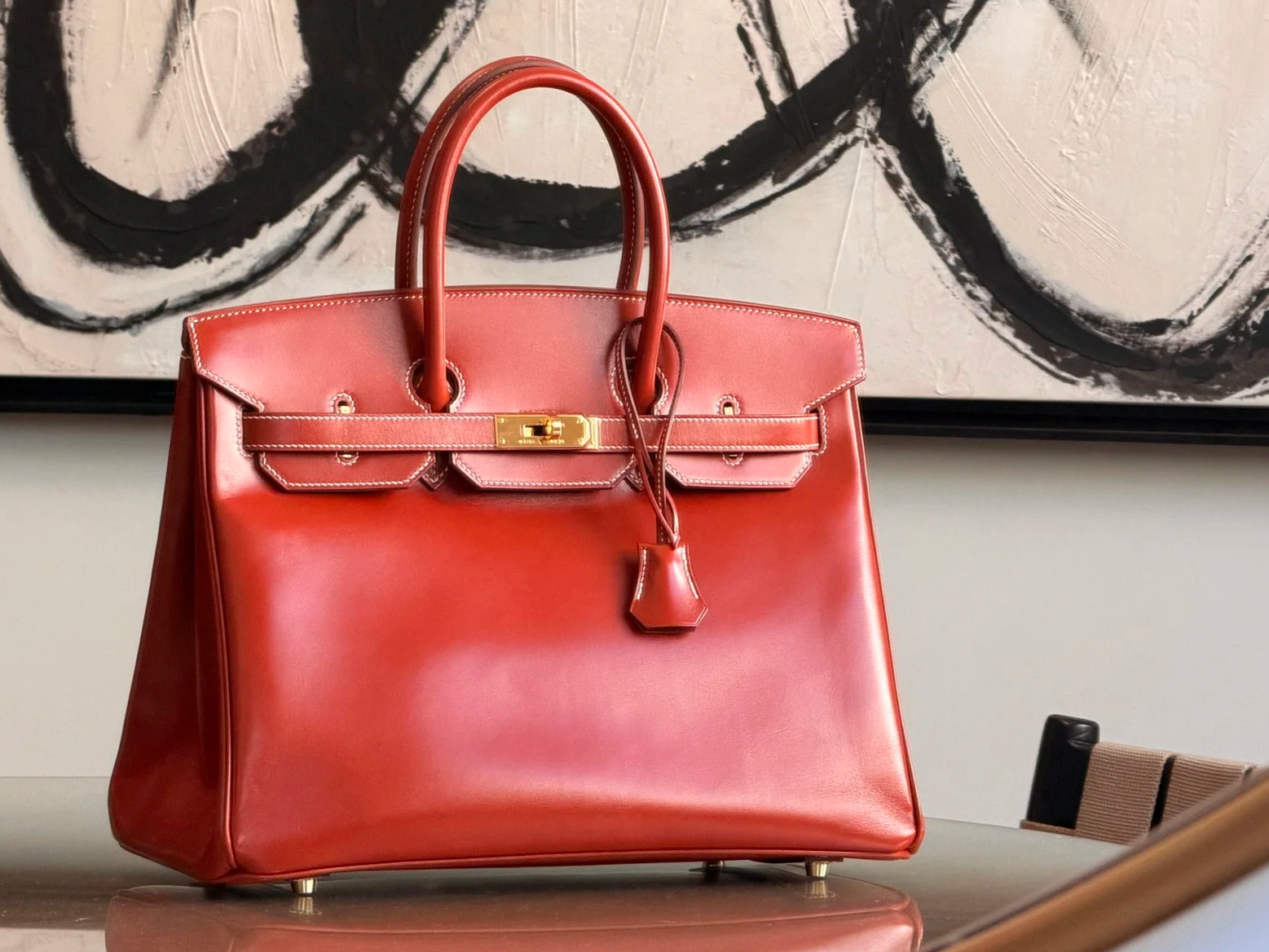 A red Hermes Birkin with gold hardware sitting on a table.
