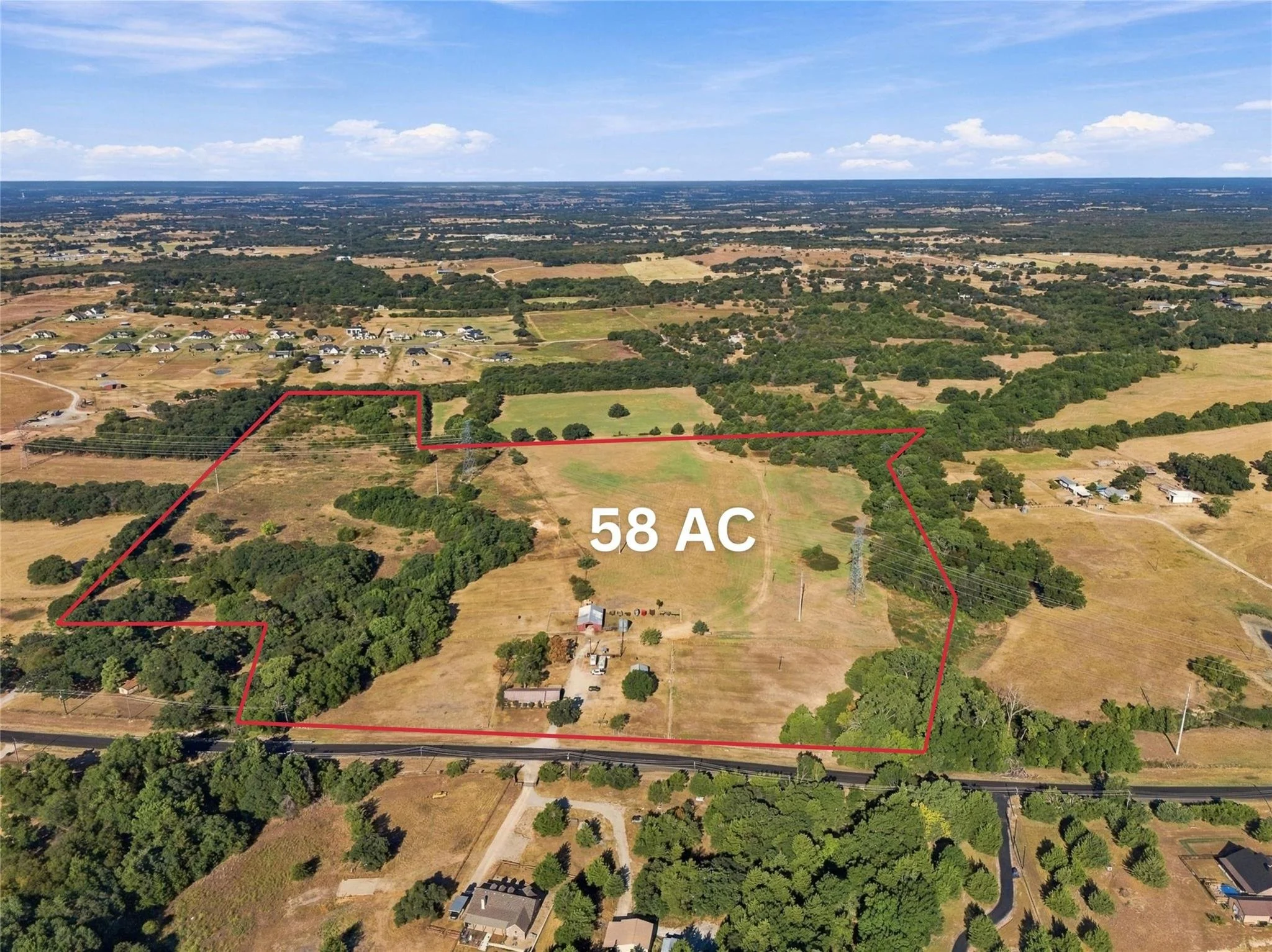 Aerial view of farmland with a plot outlined in red, indicating 58 acres of land, surrounded by trees, residential homes, and open fields under a blue sky with scattered clouds.