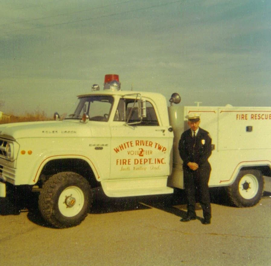 A firefighter in uniform standing next to a vintage White River Township fire rescue truck.
