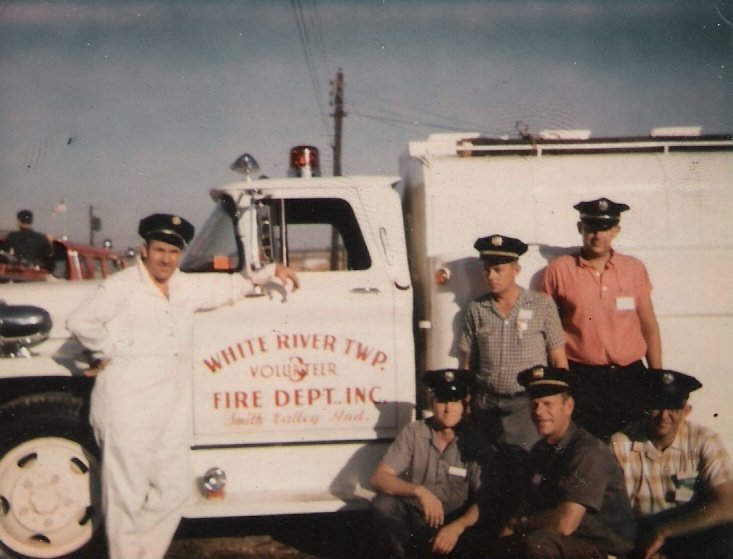 Group of five firefighters in uniform posing next to a fire truck with 'White River Twp. Volunteer Fire Dept Inc.' painted on the door.