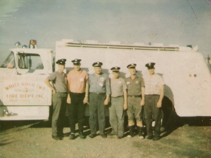 Seven firefighters in uniform standing in front of a fire truck. The truck has 'White River Fire Dept. Inc.' written on the side.