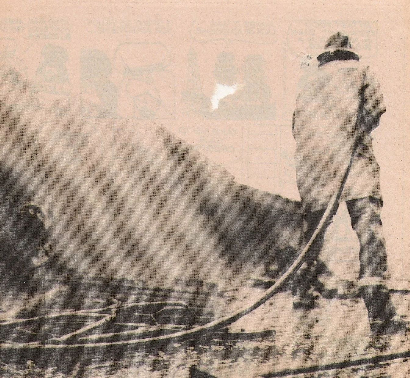A person wearing a coat and boots, viewed from behind, is holding a hose and spraying water onto the ground in a scene with smoke or steam.