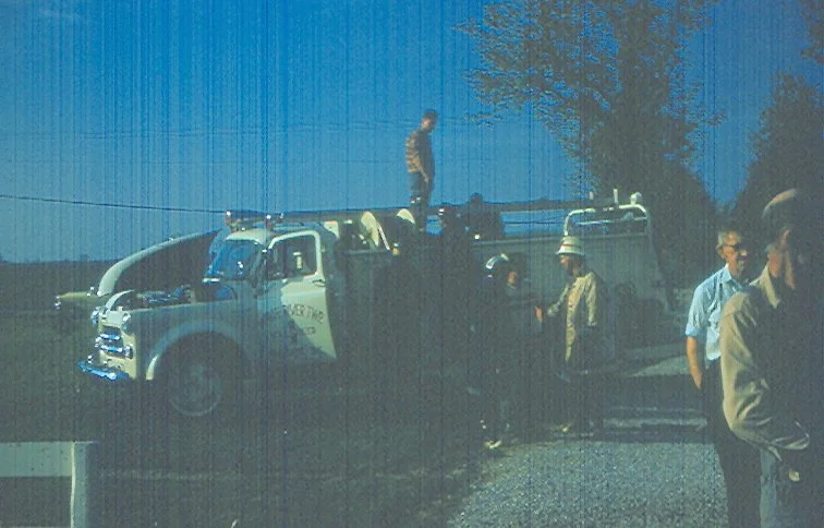 A group of people, including police officers, standing near a large truck on the side of the road during daylight.
