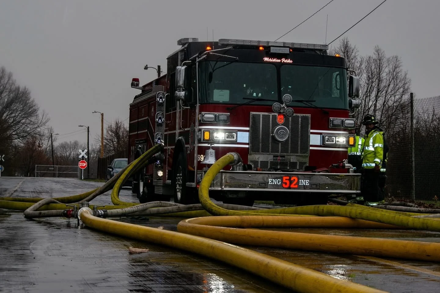 Firefighters connected hoses to a red fire truck on a wet street in an emergency scene.