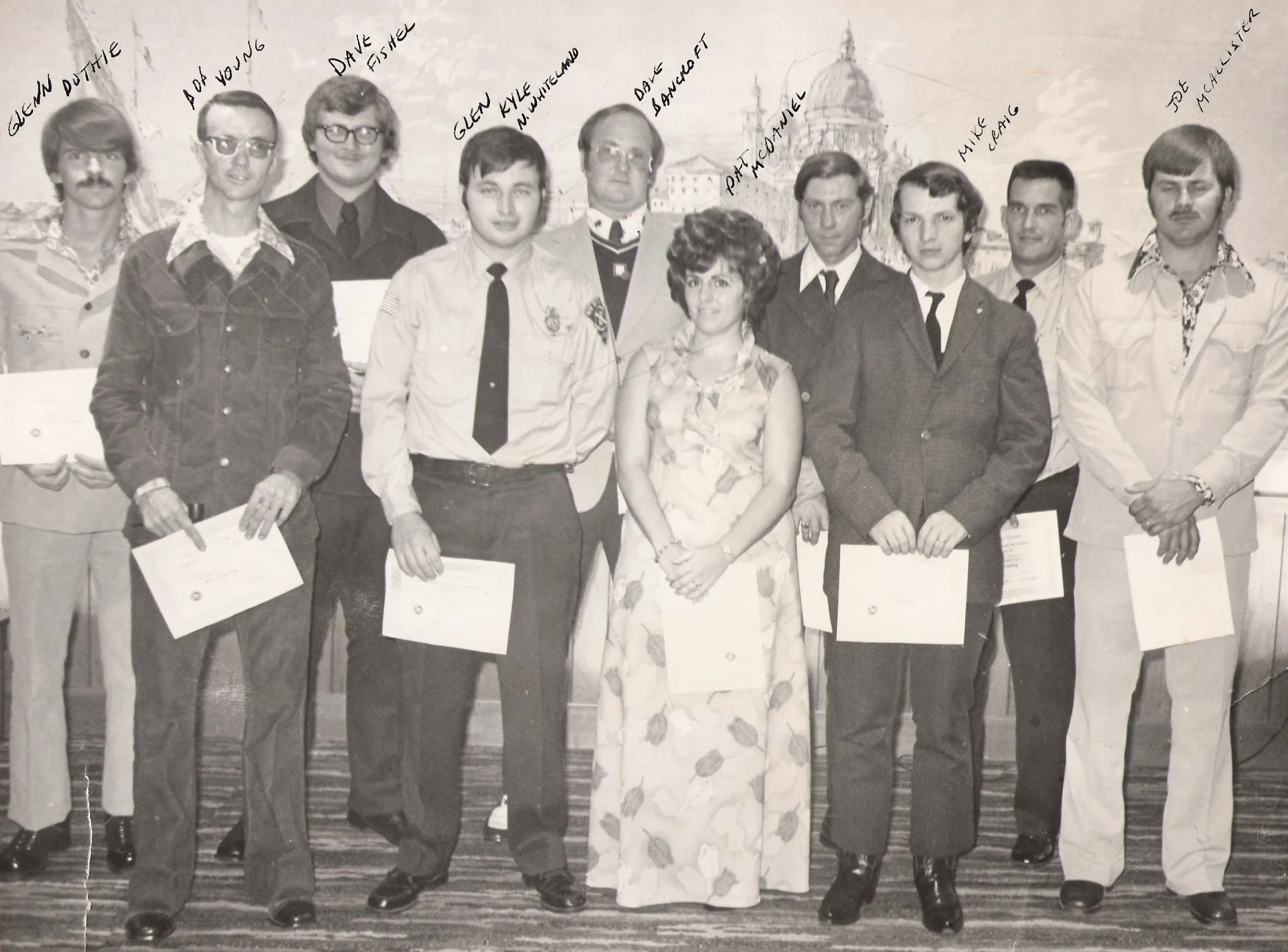 Black and white photograph of a group of people, mostly men, standing in a line, holding certificates. Several names are handwritten above their heads, including Glenn Douthie, Adolph J. Young, Dave Fister, Glenn Kyle, Dave Bancherd, Phat Connelle, M