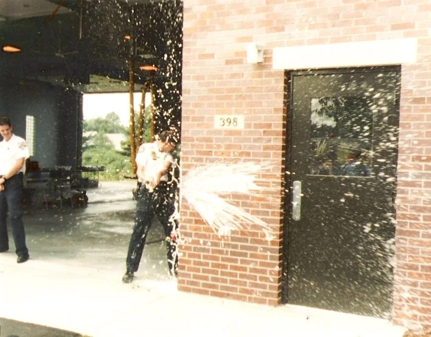 Person getting soaked by a fire extinguisher spray outside a brick building with the number 398 on it.
