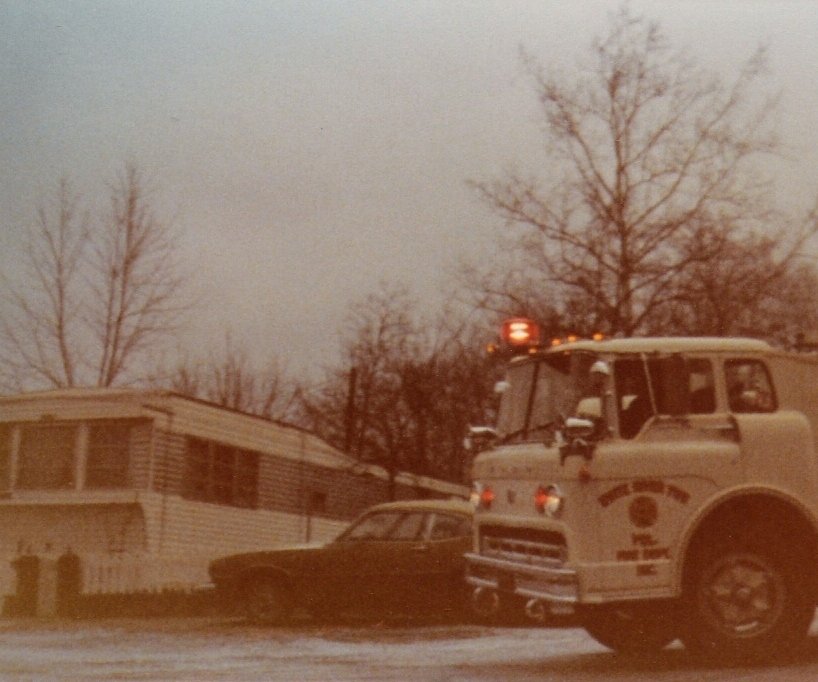 A fire truck parked on a snow-covered street near a house with leafless trees in the background.