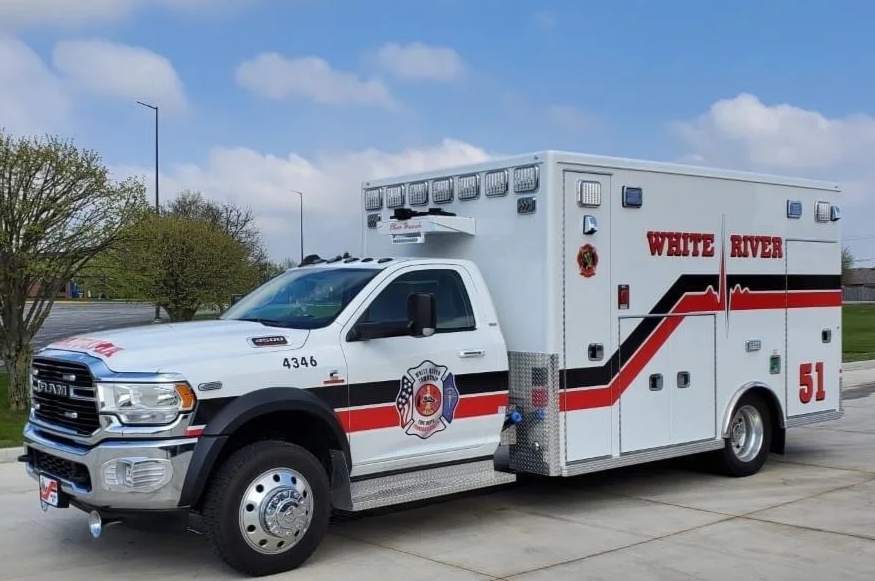 White River fire emergency vehicle with rescue department logo, parked on a street with trees and clouds in the background.