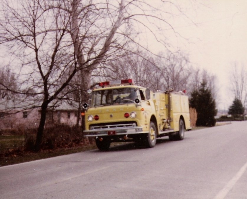Yellow vintage fire truck parked near leafless trees along a rural road.
