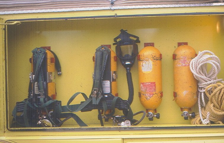 Storage compartment containing two breathing masks, two orange cylinders, and tied ropes.