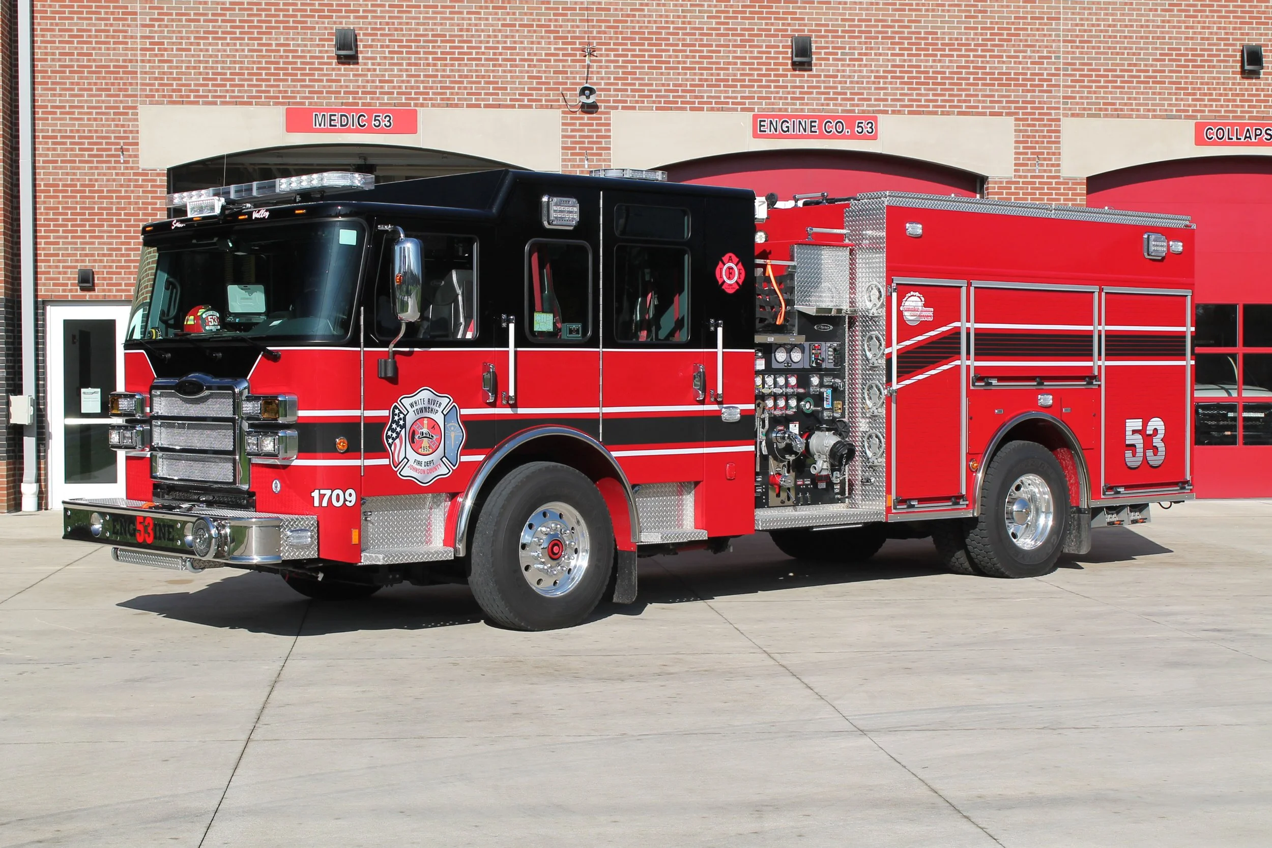 Red and black fire truck parked outside fire station with brick walls and garage doors.