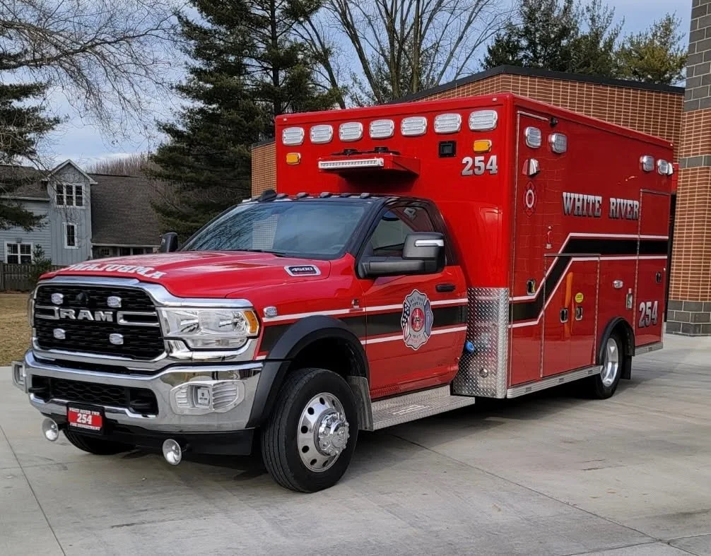 Red fire truck with white and black stripes parked outside a building with trees in the background.