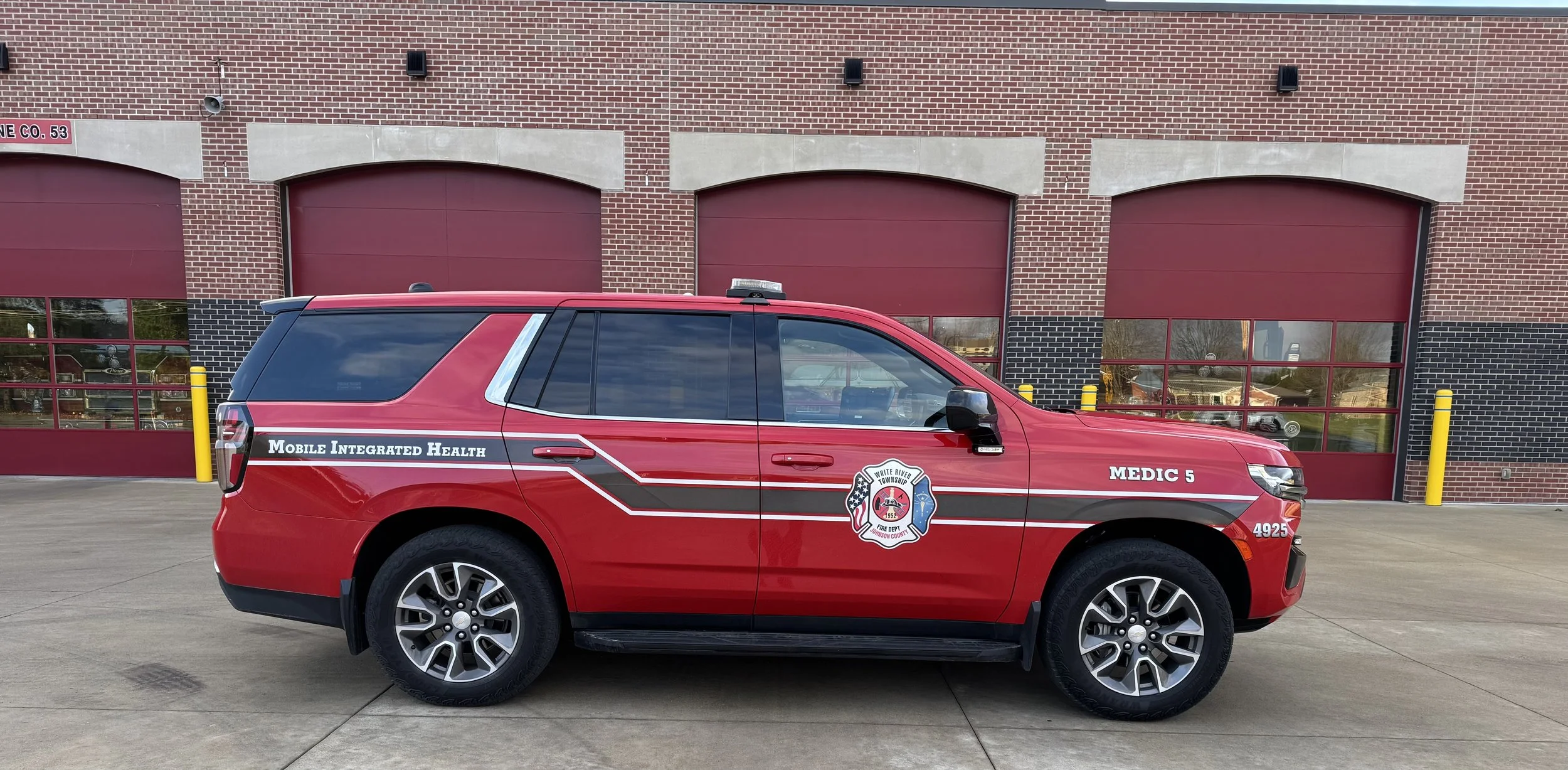 Red emergency response vehicle with 'Mobile Integrated Health' and 'Medic 5' markings parked outside a building with red garage doors.