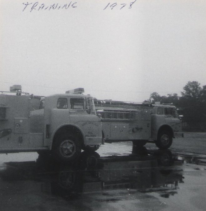 Black and white photo of a vintage fire truck from 1978, parked outdoors with a puddle reflecting its image, and handwritten notes at the top reading "Training 1978".