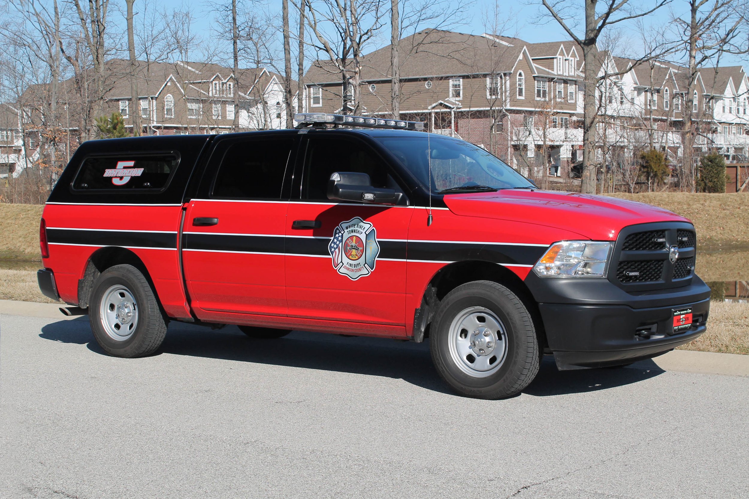 Red and black fire department utility vehicle with a Waffle River Township Fire Department logo parked on a street with residential houses in the background.