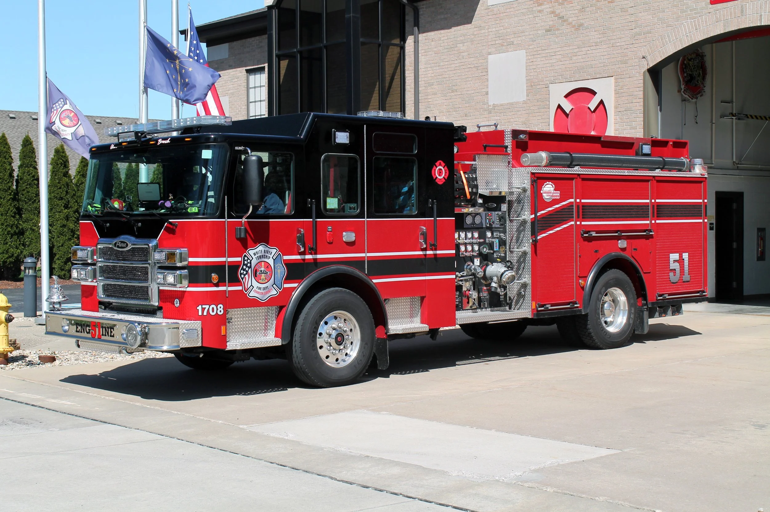 A red and black fire truck parked outside a brick building, with flags flying behind it.