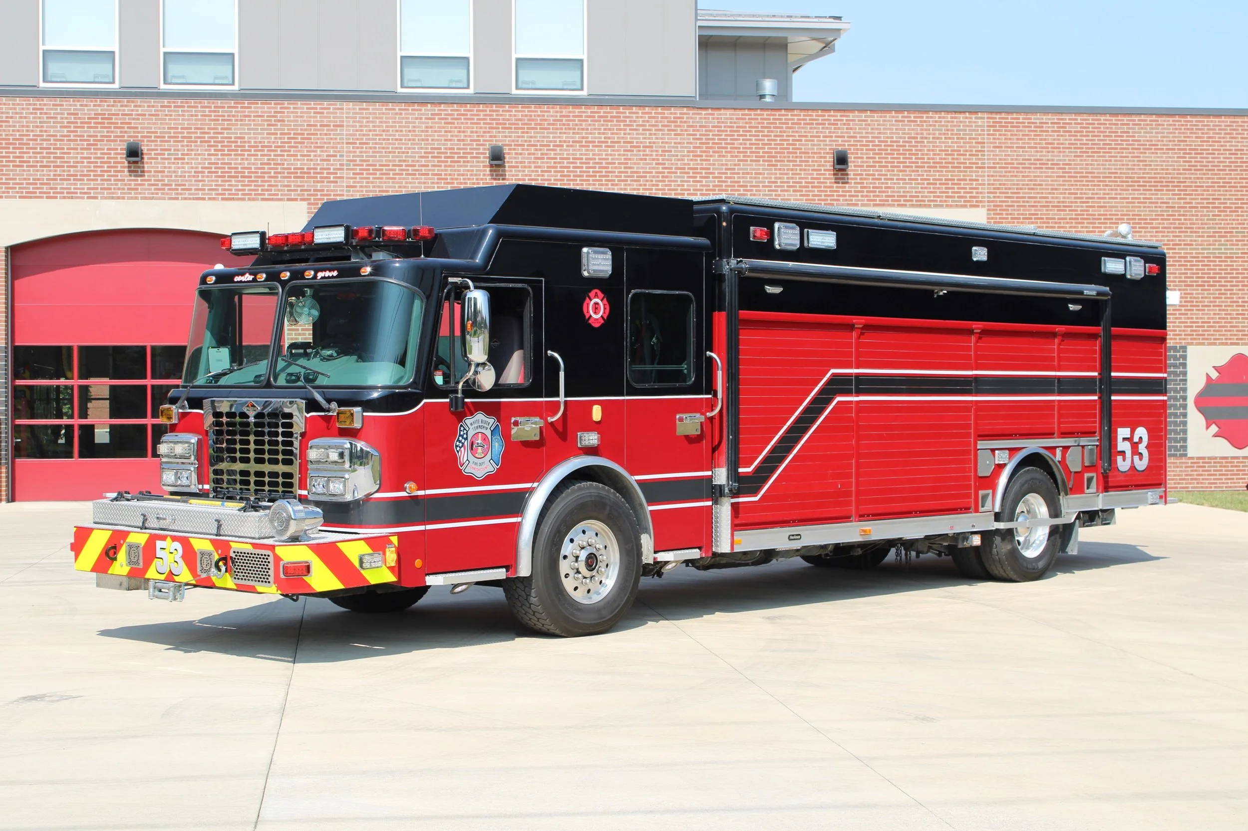 Red and black fire truck parked outside a fire station building with red garage doors.