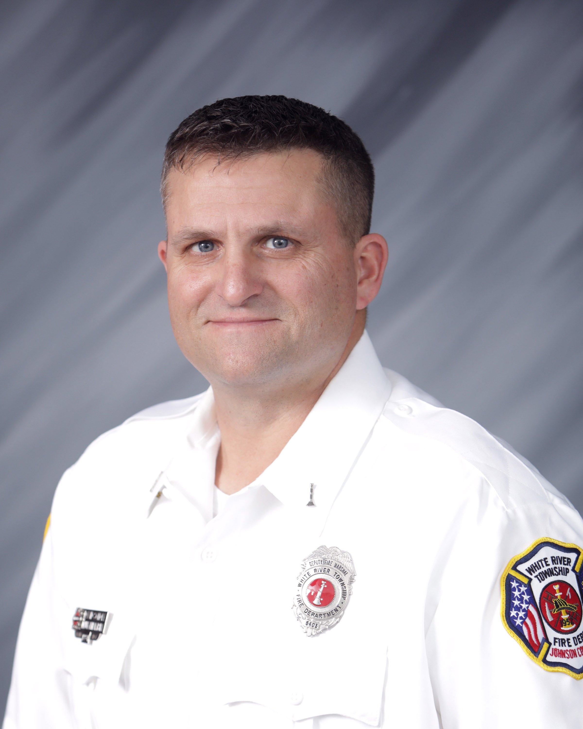 Portrait of a firefighter in uniform, with badges and patches, against a gray background.