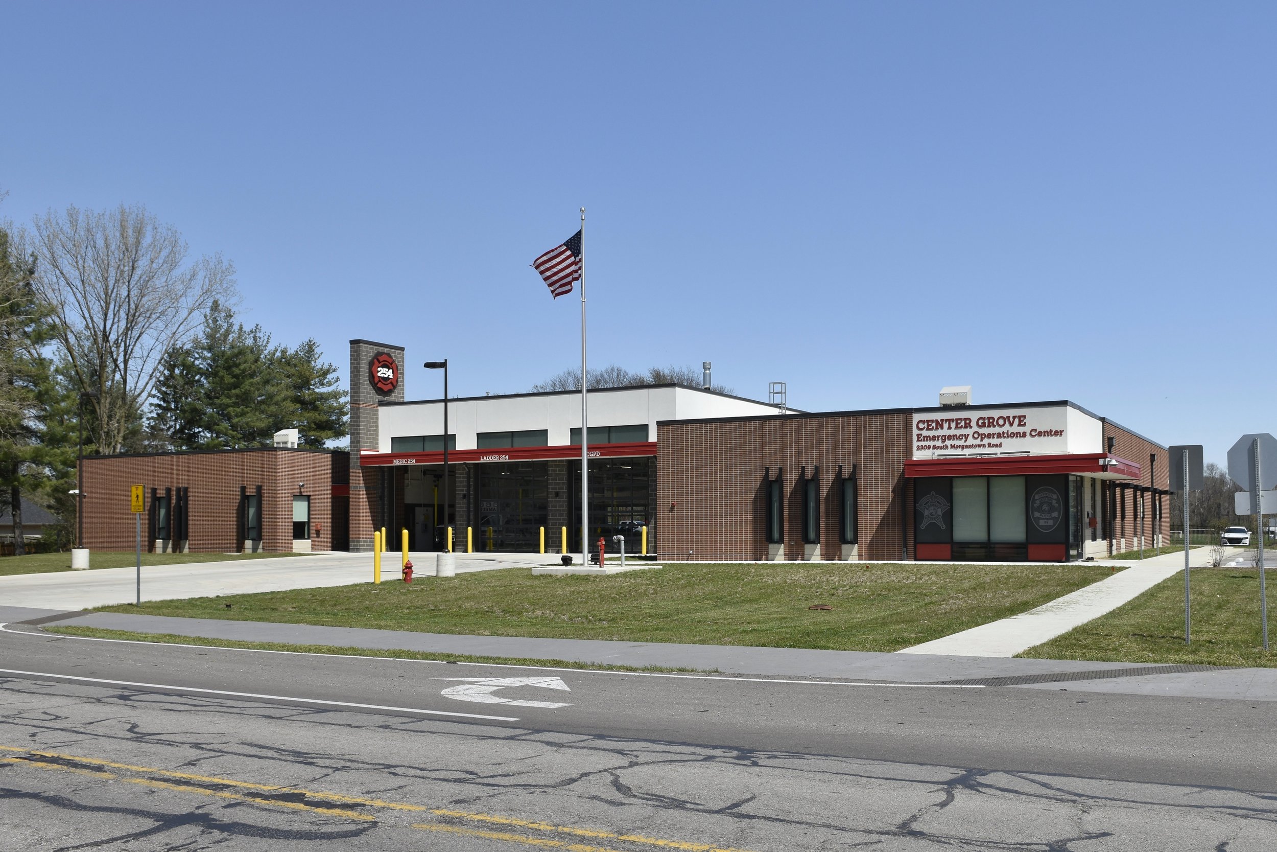 Front view of the Center Grove Emergency Operations Center building with a flagpole displaying the American flag, a brick exterior, and signage indicating it is an emergency center, located at 2300 South Morgantown Road.