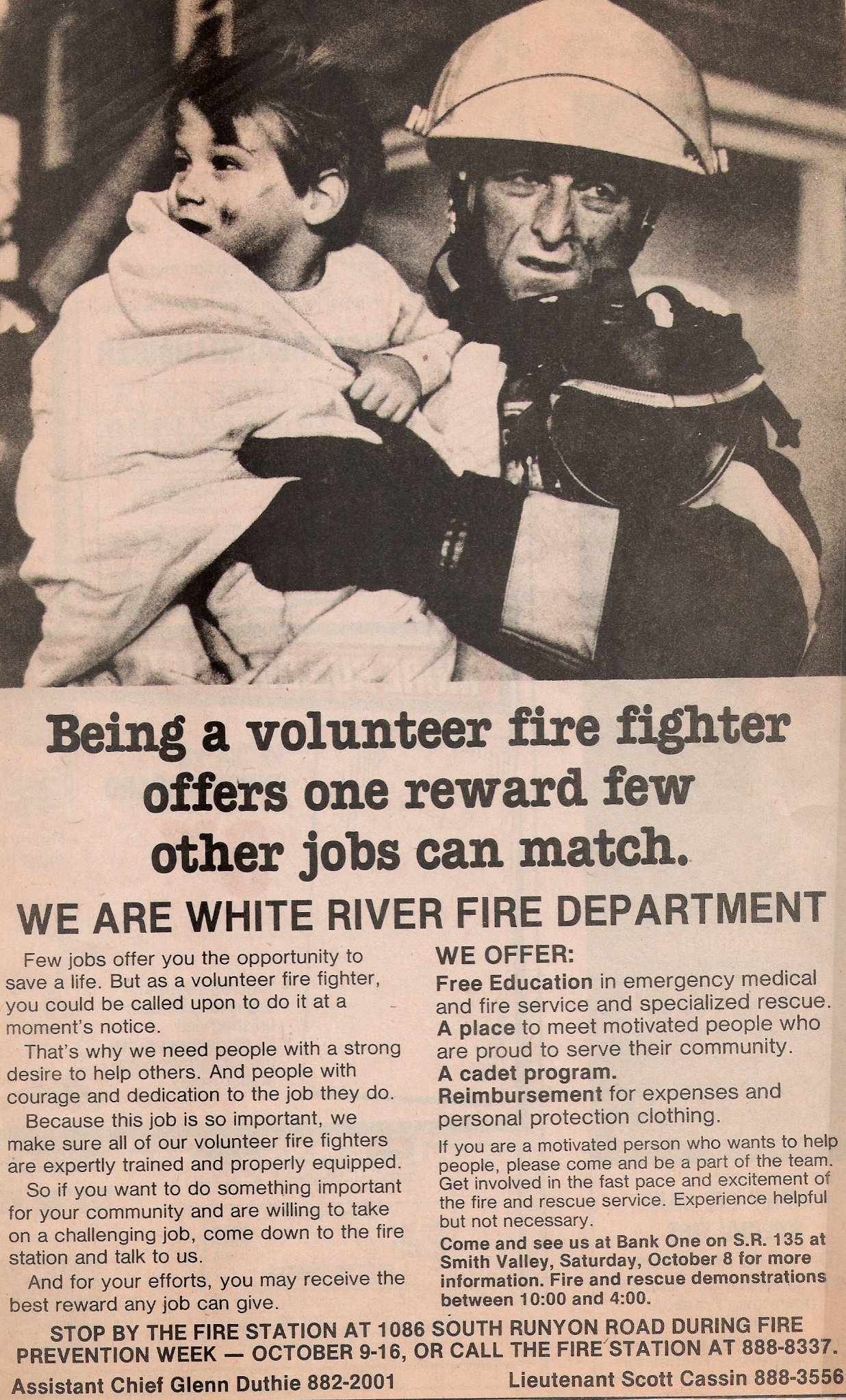 A firefighter in uniform holding a young child, both looking serious. The child is wrapped in a blanket.