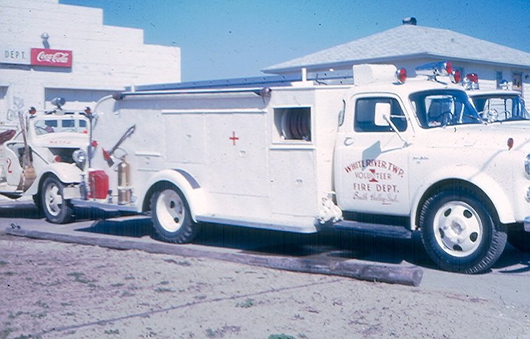 Vintage red cross fire truck parked outside a building with a Coca-Cola sign on the wall.
