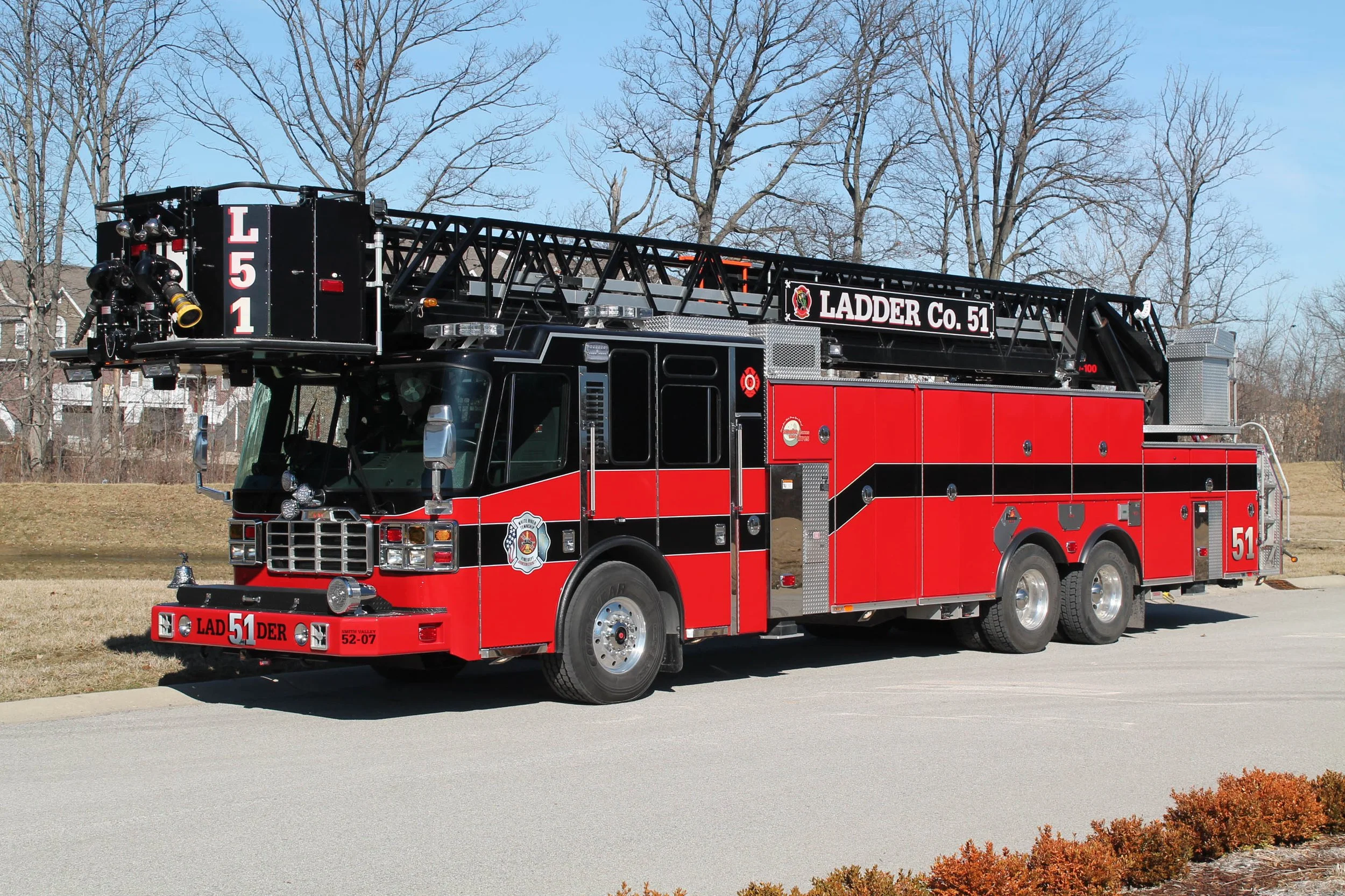 Red fire truck with a ladder on top parked on a street with trees and a clear sky in the background.