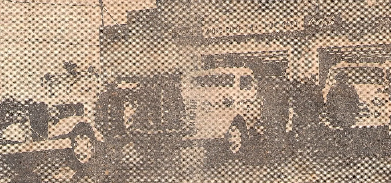 Black and white photo of vintage fire trucks and firefighters standing in front of a fire station with a sign reading 'Wright At Your Service'.