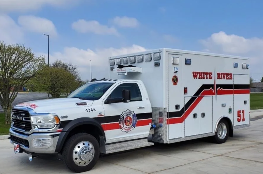 White River Fire Department ambulance truck parked on a concrete surface with trees and a cloudy sky in the background.