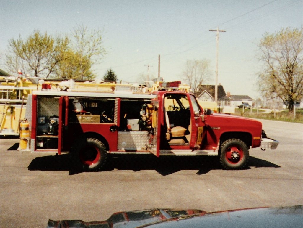 Red fire truck parked outdoors on a clear day with trees and houses in the background.
