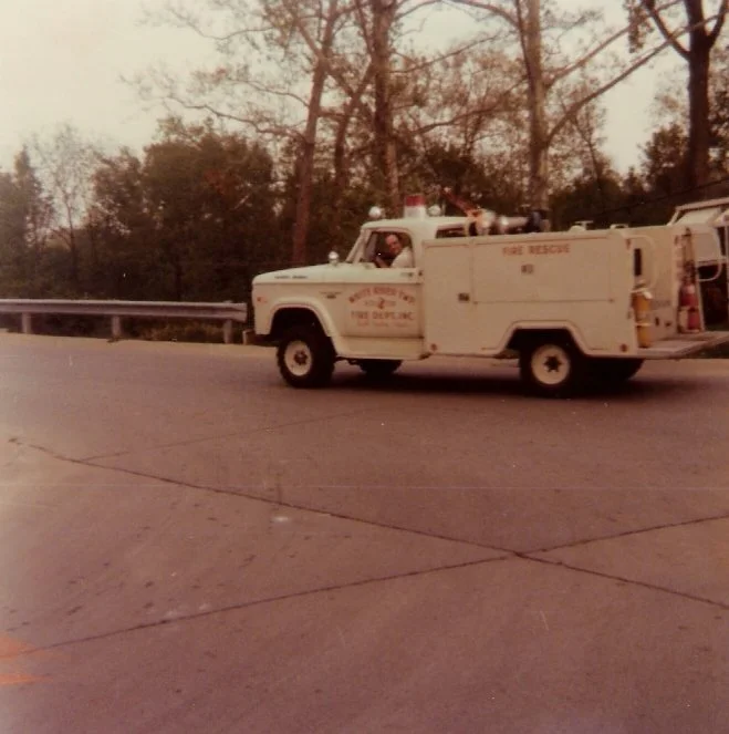 Vintage fire rescue truck parked on the side of a road with trees in the background.