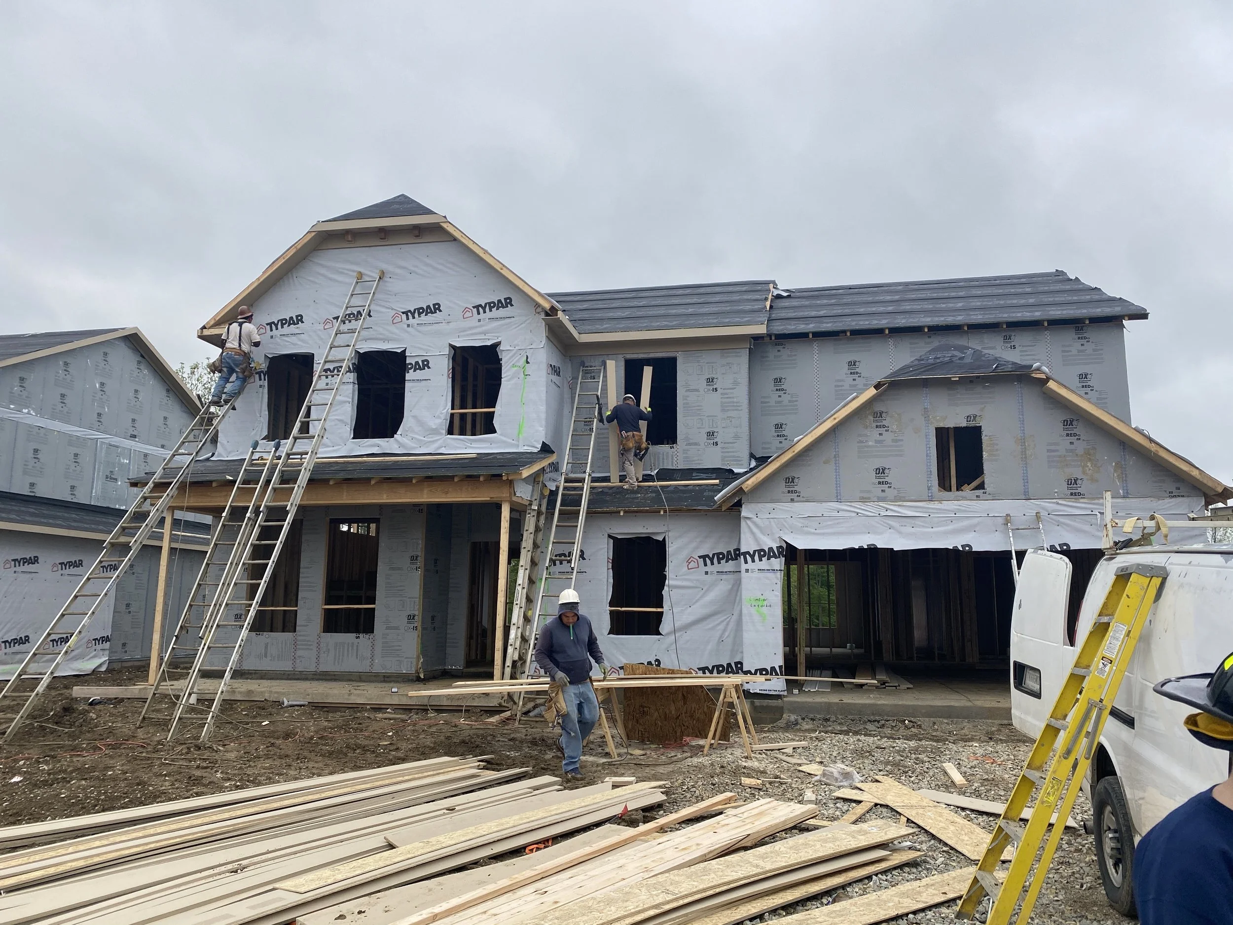 Construction workers building a multi-story house, with scaffolding and ladder, and construction materials on the ground.