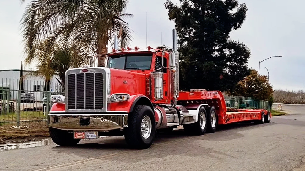 Red semi-truck from H&S Heavy Haul parked on a street with trees and fence in the background.