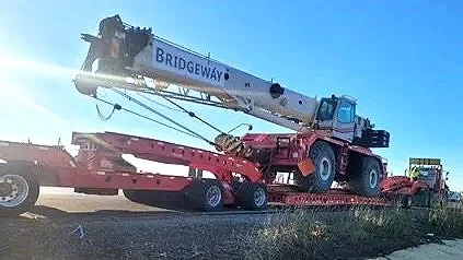 A large crane labeled 'Bridgeway' on a flatbed truck from H&S Heavy Haul, positioned on train tracks during daylight.