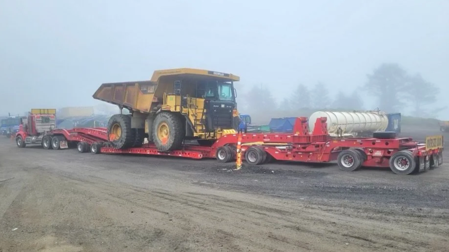 Large yellow dump truck being transported on a red lowboy trailer from H&S Heavy Haul.