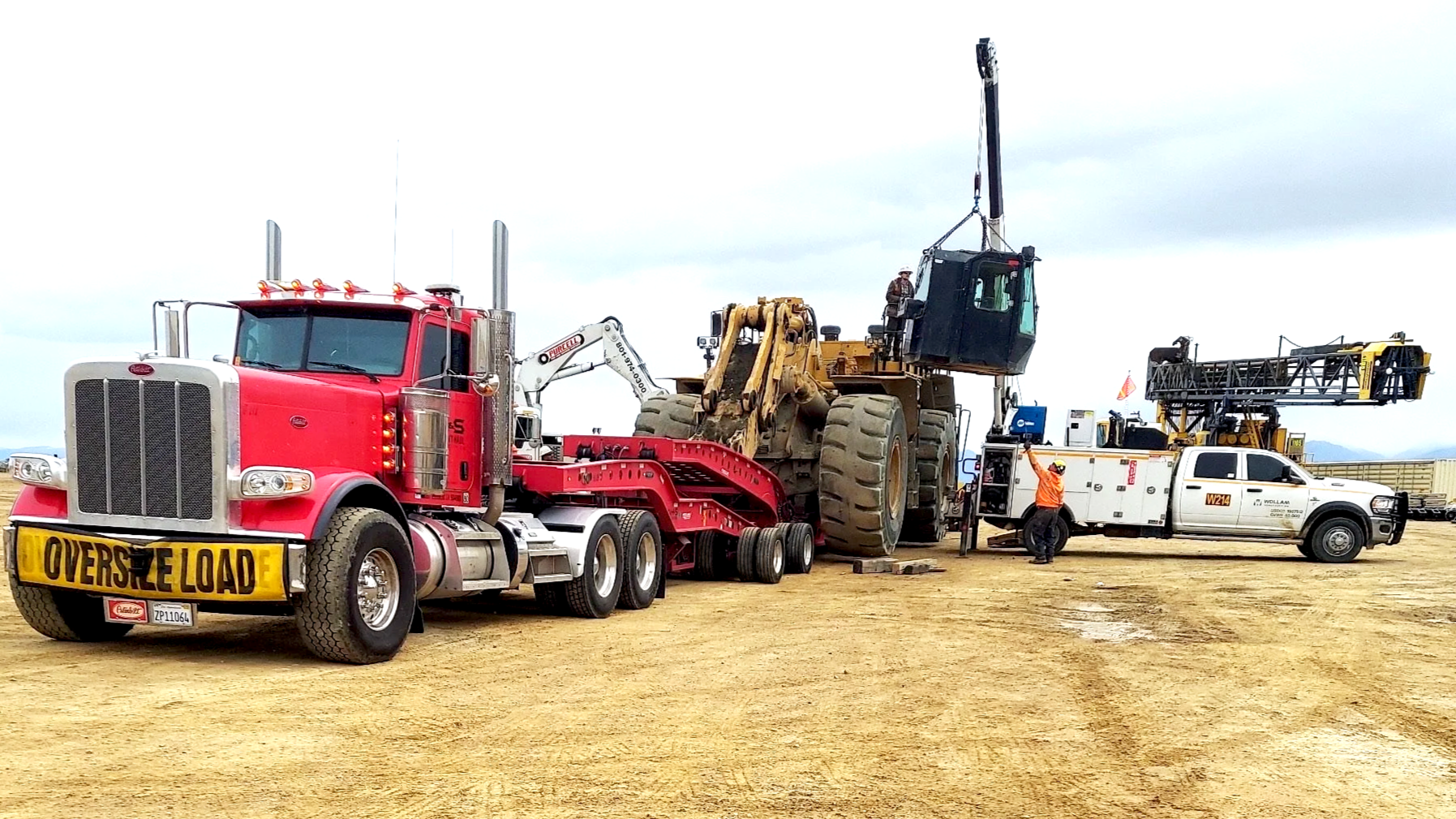 A large red semi-truck from H&S Heavy Haul with a yellow sign that reads 'OVERSIZE LOAD' is transporting a giant construction vehicle.
