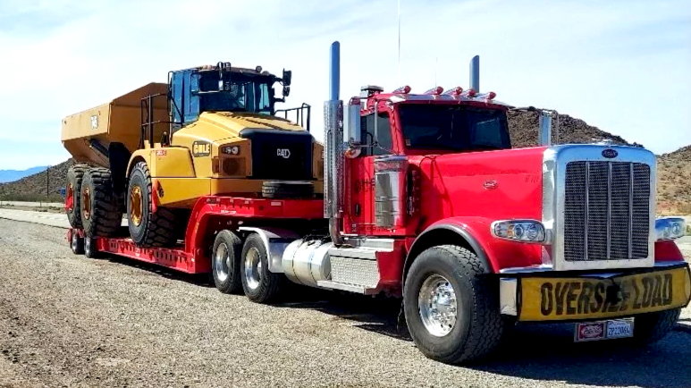 A red semi-truck from H&S Heavy Haul carrying a yellow bulldozer on a flatbed trailer on a desert highway.