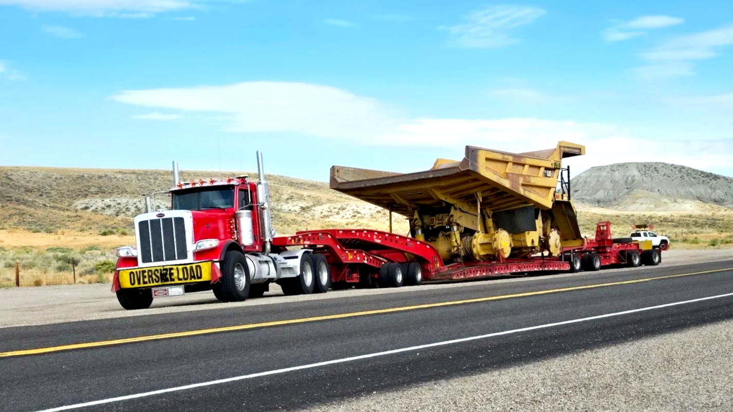 H&S Heavy Haul Truck transporting oversized machinery on a highway with desert landscape in background.