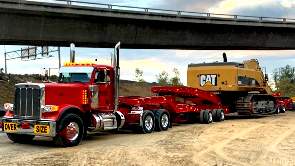 A red semi-truck from H&S Heavy Haul  transporting a large Caterpillar bulldozer on a flatbed trailer.