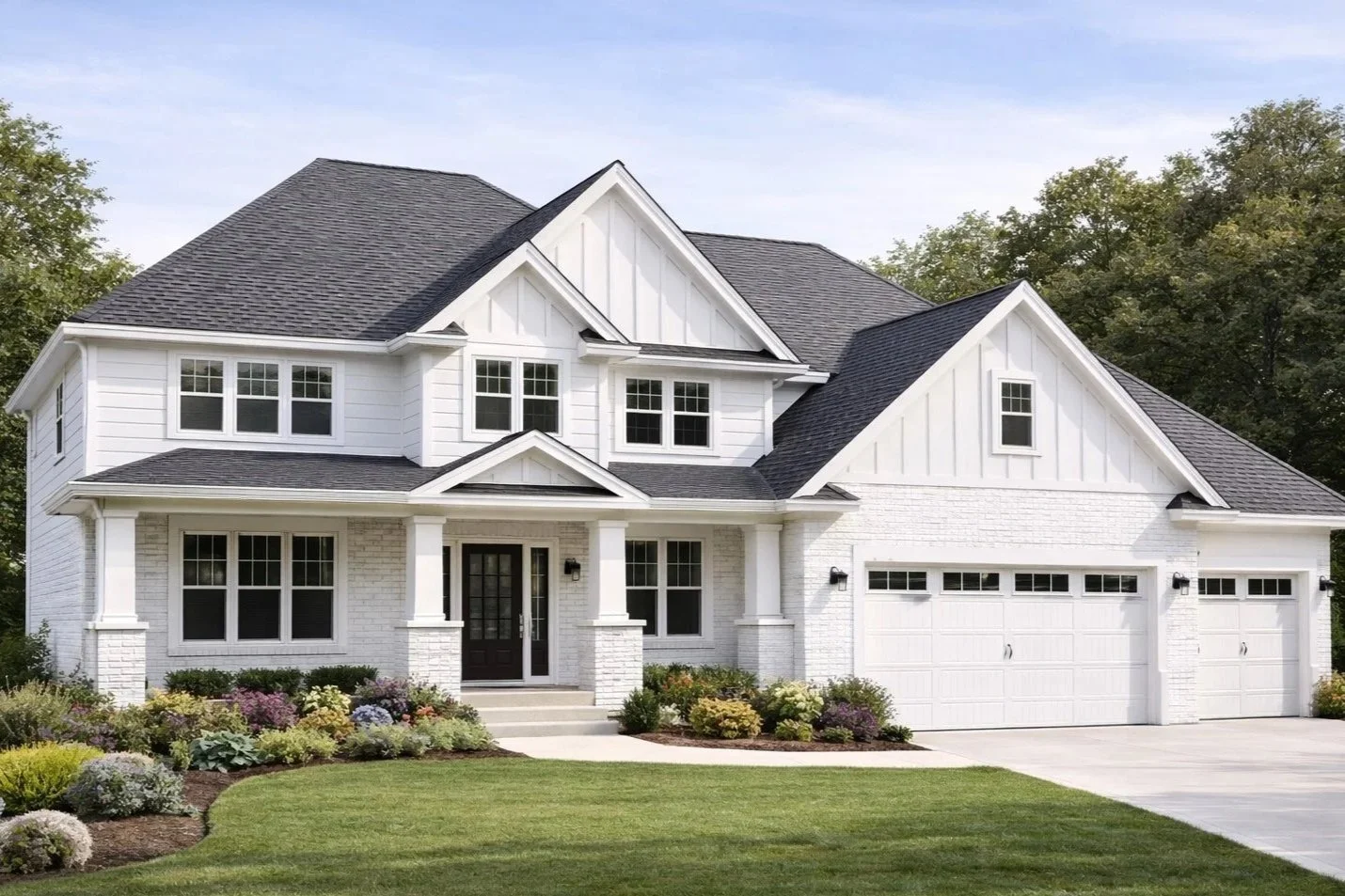White two-story house with black roof, front porch with columns, multiple windows, attached garage, landscaped lawn and garden.