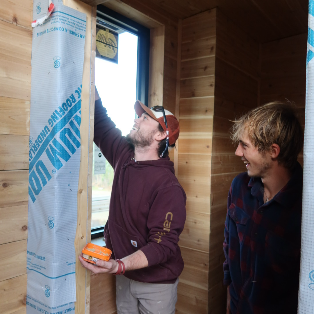 Wooden sauna interior with bench seating, a heater filled with stones, and a bucket with a ladle.
