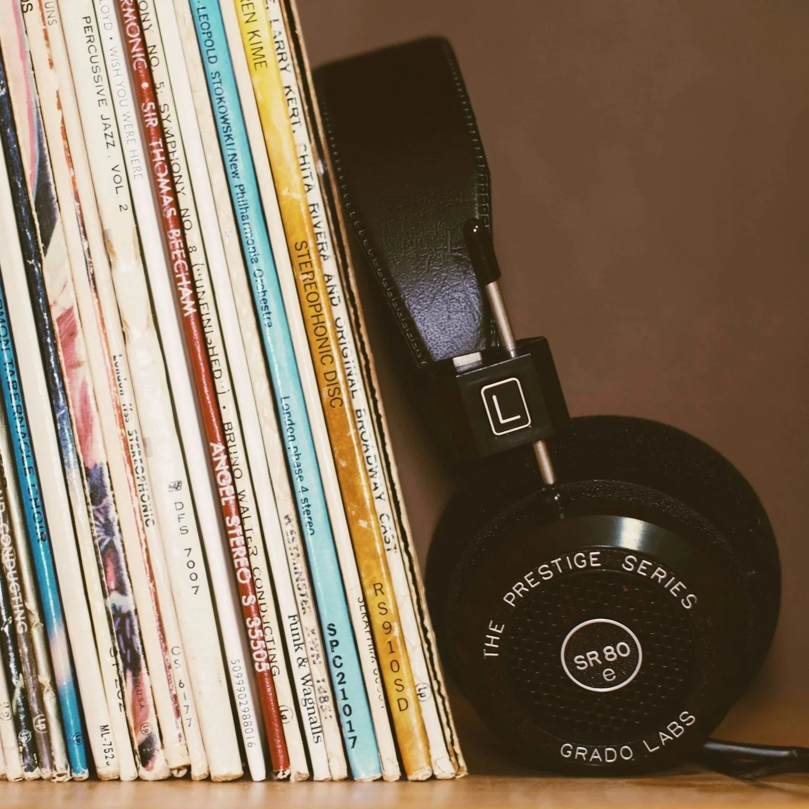 A row of colorful music magazines or books standing upright on a shelf with a black speaker with silver accents next to them.