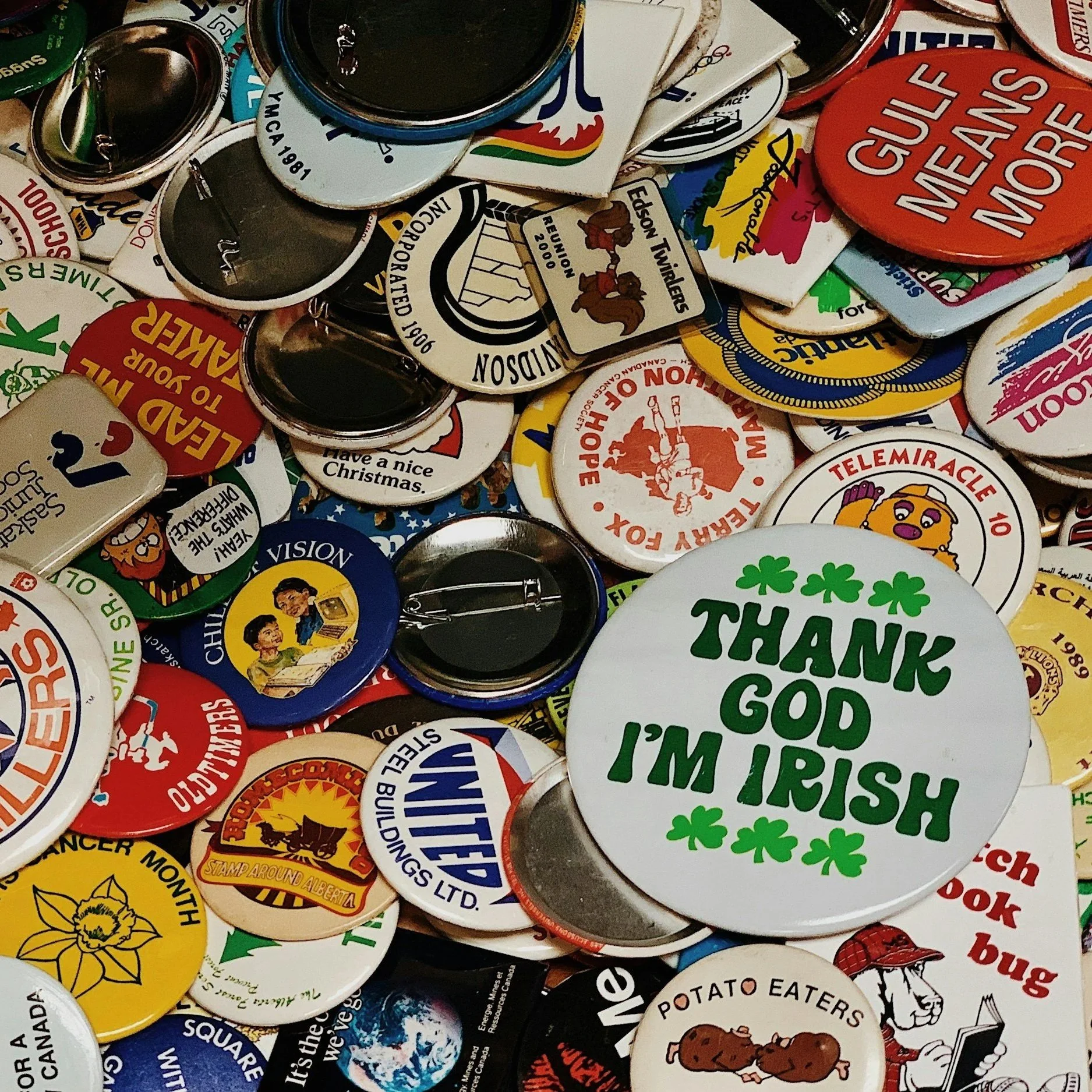 A collection of various colorful badges and pins with different slogans, logos, and images, including messages like "Thank God I'm Irish" and "Head to your super."