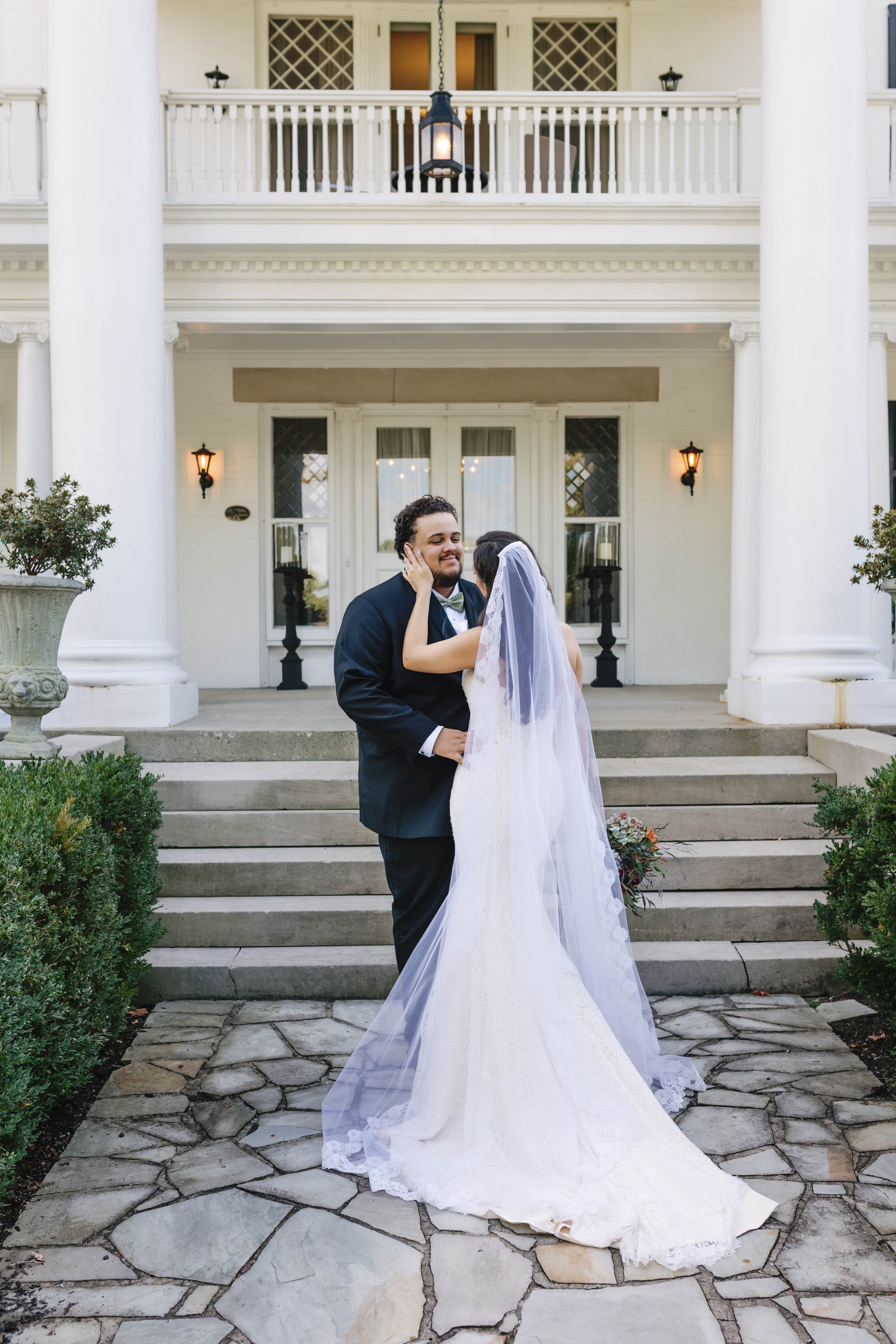 A bride and groom sharing an intimate moment on the steps of a large, elegant white house. moundale manor historic kentucky wedding venue winchester kentucky 
