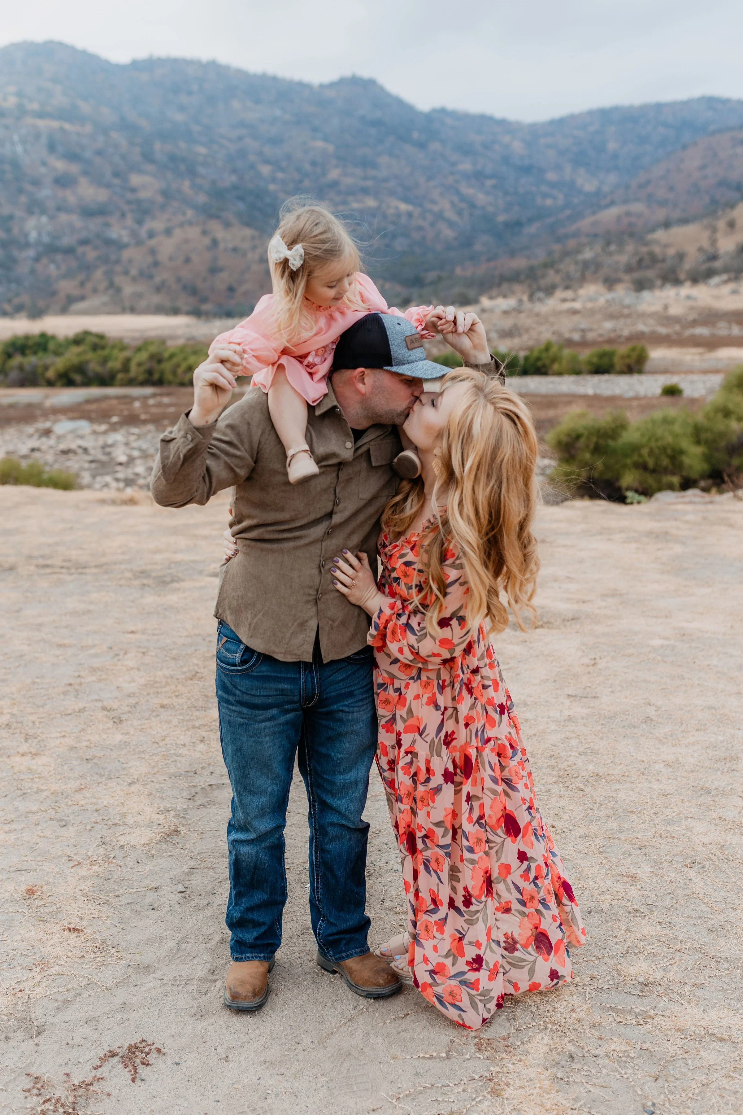 A family of three sharing a kiss outdoors with mountains in the background.   lexington kentucky family photographer storytelling portraits