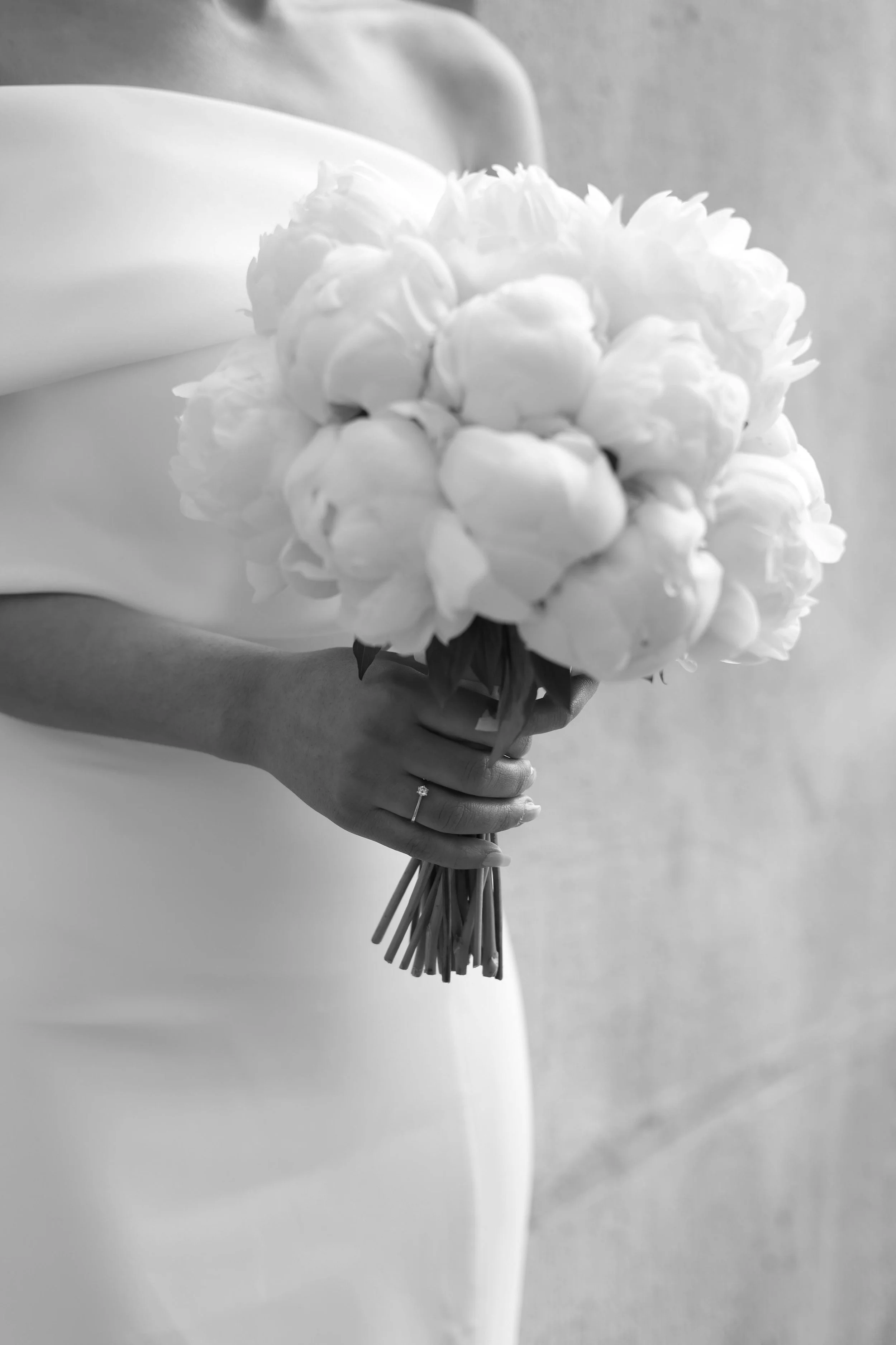 A woman in a white dress holding a large bouquet of white flowers, with a wedding ring on her left hand.