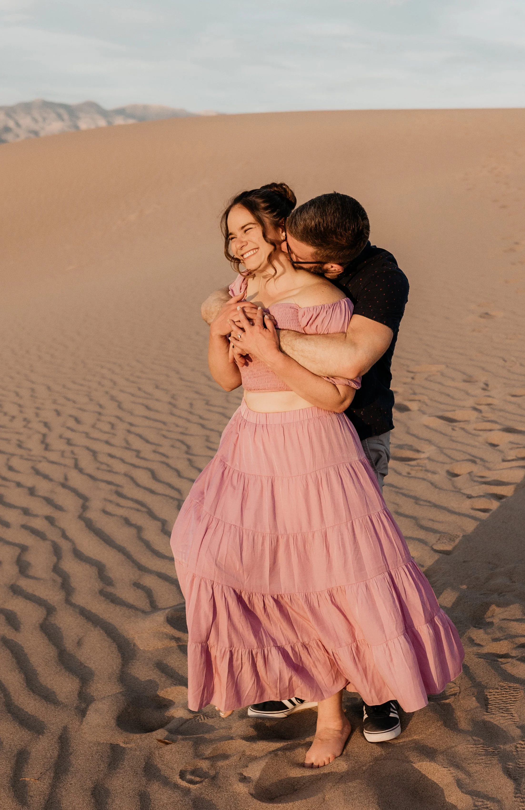 A couple embraces and kisses in a desert landscape during sunset, with sand dunes in the background death valley national park elopement