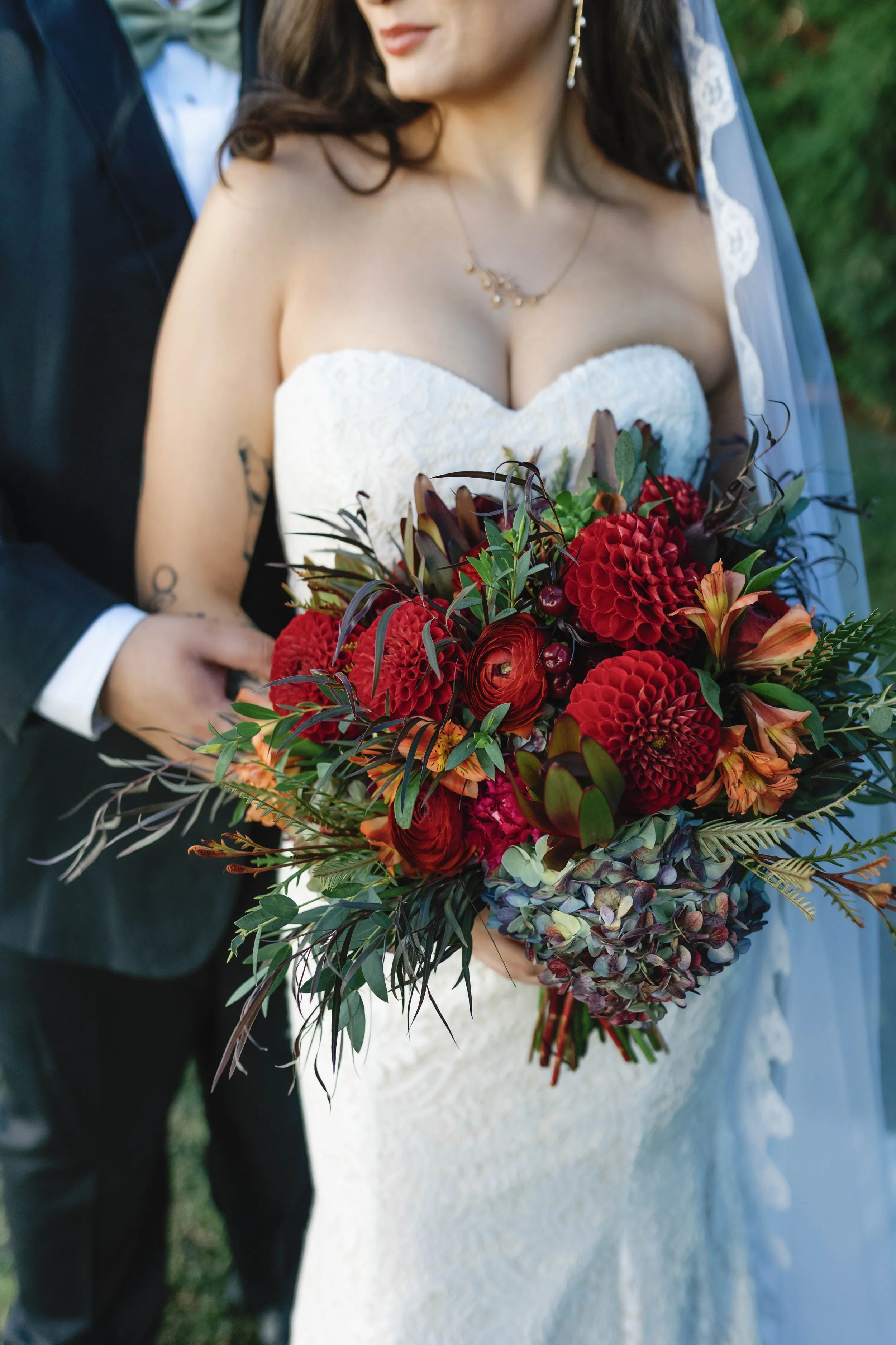 A bride holding a large bouquet of red and purple flowers at her wedding, with her groom standing behind her, partially visible. moundale manor historic kentucky wedding venue winchester kentucky 